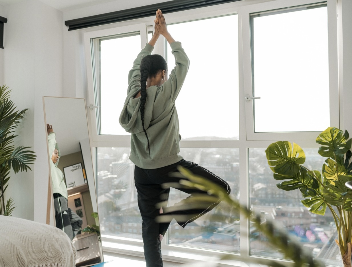 Student doing a yoga tree pose in her room looking out of the window